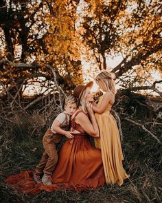 two women and a boy are sitting on the ground in front of some trees with their faces close to each other