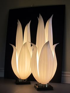 three white lamps sitting on top of a table next to a black framed artwork piece