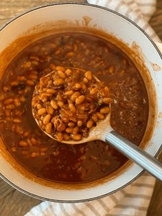 a spoon full of beans in a pot on top of a wooden table next to a napkin