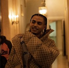 a man with dreadlocks standing in a hallway wearing a brown and white jacket