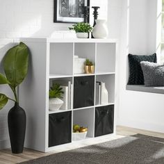 a white shelf with black bins and some plants