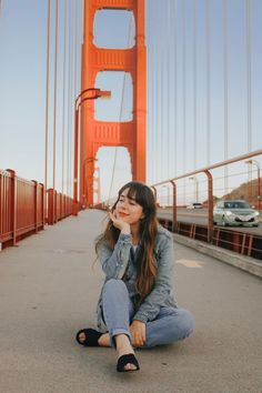 a woman sitting on the ground in front of a golden gate bridge with her eyes closed