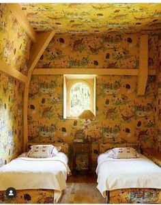 two beds in a small room with floral wallpaper on the walls and wooden floors