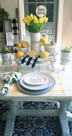 the table is set with yellow flowers and lemons in white vases, plates and napkins