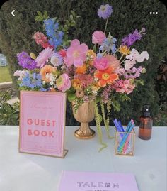 a vase filled with colorful flowers next to a guest book on top of a table