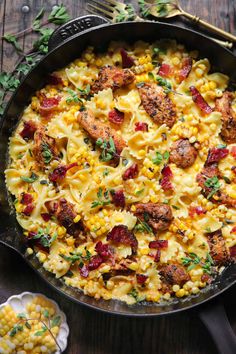 a skillet filled with pasta and meat on top of a wooden table next to utensils