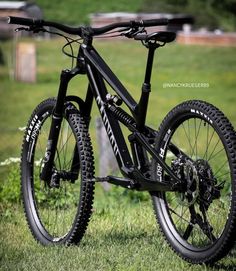 a black mountain bike parked on top of a lush green field