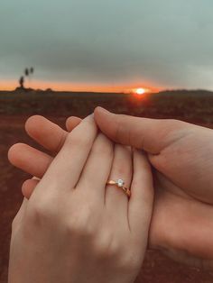 two people holding each other's hands in front of an orange sky at sunset