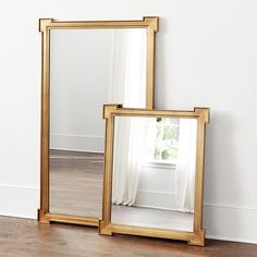 two mirrors sitting on top of a hard wood floor next to a white curtained window