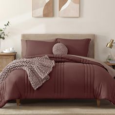 a bed with red comforter and pillows in a room next to two pictures on the wall