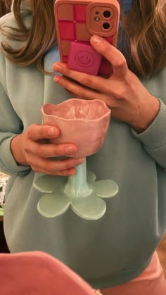 a woman taking a selfie with her cell phone while holding a pink cup in front of her