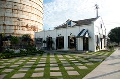 a white building sitting on top of a lush green field next to a silo