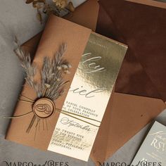 the wedding stationery is set on top of brown envelopes with gold foiling