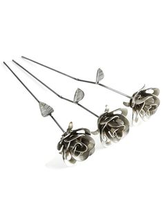 four metal roses are arranged in a row on a white surface, with one flower attached to the other