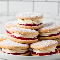 a white plate topped with cookies covered in powdered sugar and strawberry jam filled cream