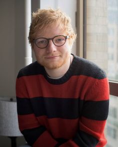 a man with red hair and glasses sitting in front of a window looking at the camera