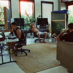 two men and a woman are sitting in an office with computer monitors on the wall