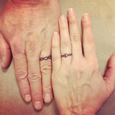 two people holding hands with tattoos on their fingers and the other hand has a ring