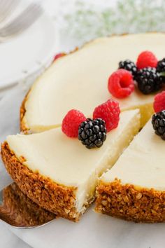 a cheesecake with berries and raspberries on top is cut in half to show the filling