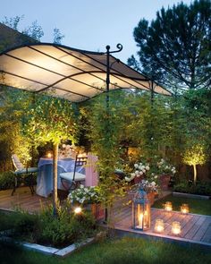 an outdoor dining area is lit up with candles and flowers on the decking, surrounded by greenery