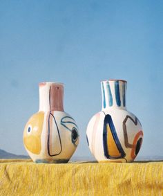 two vases with faces painted on them sitting next to each other in front of a blue sky