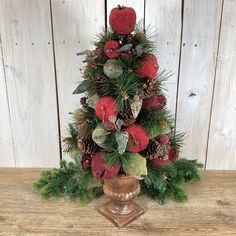 a small christmas tree with pine cones and berries on it's top, in front of a wooden wall