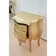 an antique style dresser with three drawers and gold paint on the top, in front of a white wall