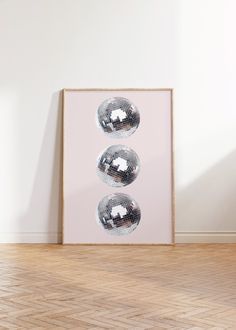 three shiny disco balls are hanging on the wall in front of a wooden floor and white walls