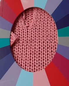 a pink knitted object in front of a multicolored background with a circular hole