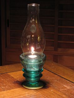 a glass vase sitting on top of a wooden table with a lit candle in it