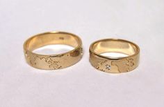 two gold wedding rings with the map of the world engraved on them, sitting next to each other