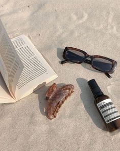 an open book, eyeglasses, and some sand on the beach next to it