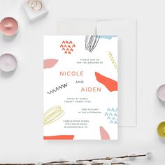 a wedding card with an abstract design on the front and back, sitting next to candles