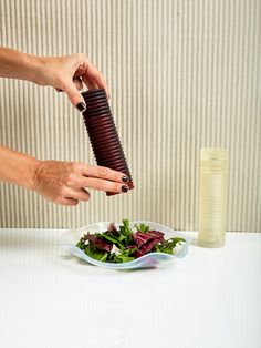 a woman is holding an object over a bowl of salad