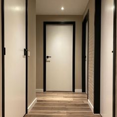 an empty hallway with white walls and black trim on the doors, leading to another room