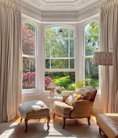 a living room filled with lots of furniture next to two large windows covered in curtains