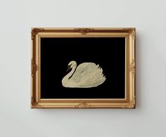 a white swan floating in the water on a black and gold framed wall art piece