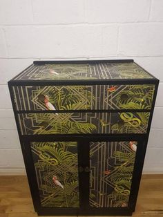 a black and green painted cabinet with birds on the front, surrounded by palm leaves