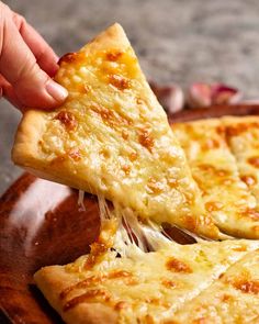 a person taking a slice of cheese pizza from a wooden platter on the table