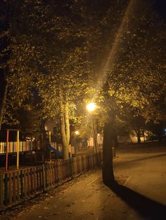 a street light shines brightly on the trees in front of a fenced area