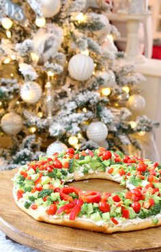 a pizza with veggies and tomatoes on it sitting in front of a christmas tree