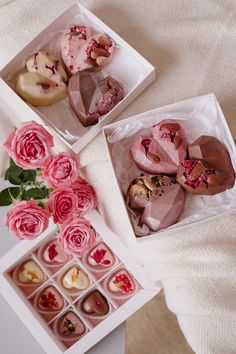 three boxes filled with assorted pastries on top of a white table next to pink roses