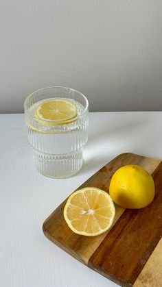 a wooden cutting board topped with sliced lemons next to a glass filled with water