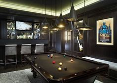 a pool table in the middle of a room with bar lights and chairs around it