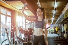 a woman taking a selfie with her cell phone in a gym room full of exercise equipment