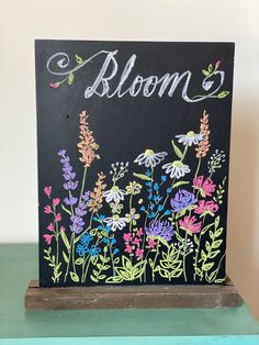 a chalkboard sign that says bloom with flowers painted on the front and back side