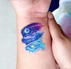 a person with a tattoo on their arm holding up the wrist that is covered in watercolors