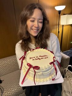 a woman holding a cake with the words happy birthday written on it in red ribbon