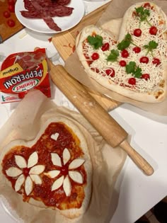 two heart shaped pizzas sitting on top of a table next to other food items