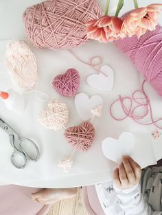 yarn, scissors and other crafting supplies are on a table with pink flowers in the background